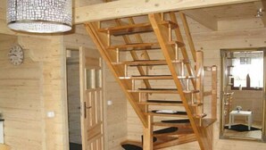 Et træinteriør med en spiraltrappe, et ur og et spejl der reflekterer et rum med en stol og et bord.