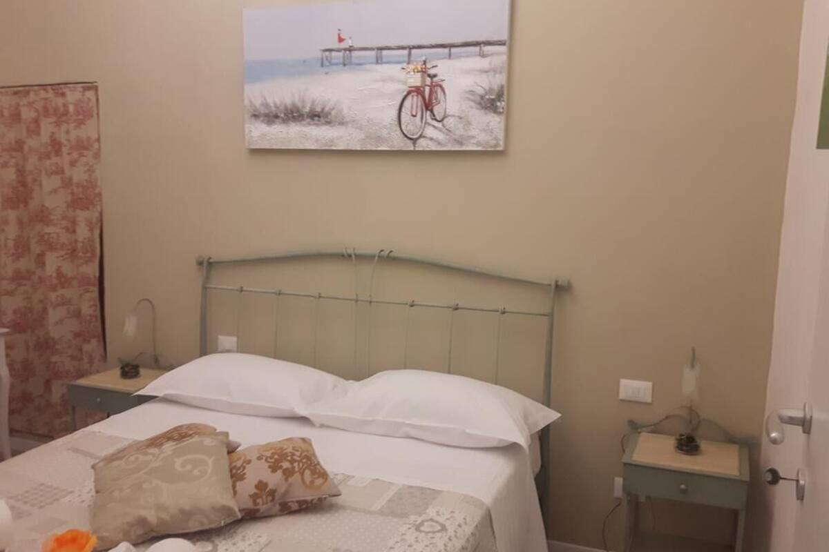 Une chambre d’hôtel avec un lit, une table de chevet, une commode et un tableau représentant un vélo sur une jetée.