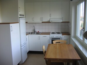 A compact kitchen with white cabinets, a sink, a stove, and a wooden table. - Volontärgatan - Visby Lägenhetshotell (Visby)