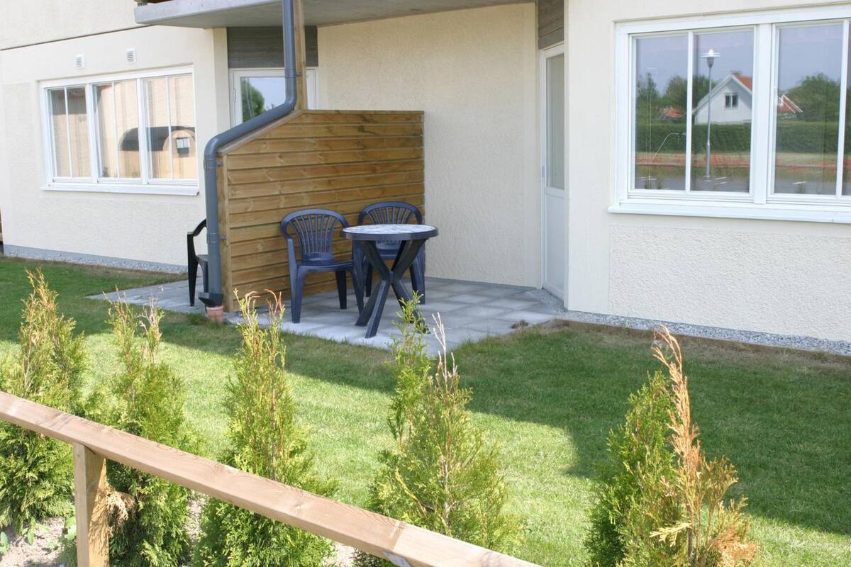 Eine Terrasse mit zwei Stühlen und einem kleinen Tisch, einem Holzzaun und einer Rasenfläche mit kleinen Pflanzen.