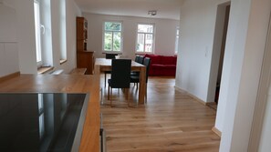 Una cocina amplia con piso de madera, un comedor con sillas y un sofá rojo al fondo.