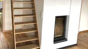 A loft-style room with a wooden ladder leading to a lofted bed, a fireplace, and a white wardrobe. - Casa Meloni (Bad Sachsa)