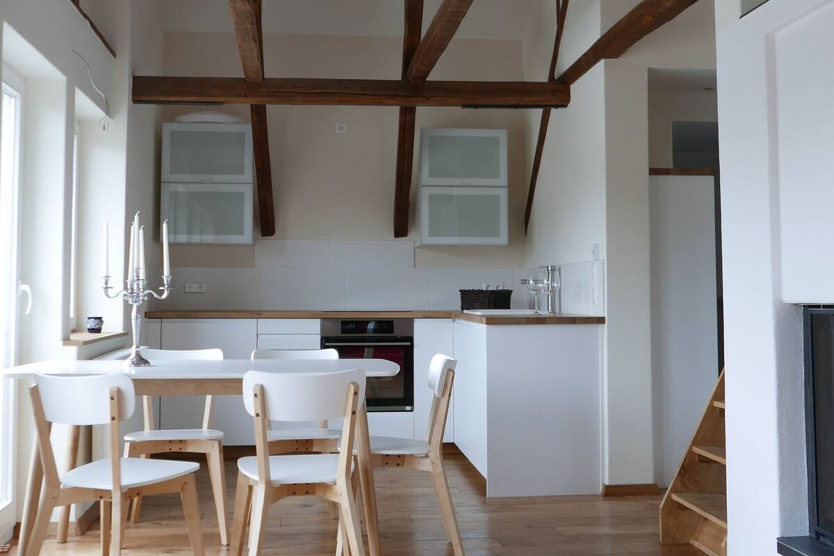 Una cocina espaciosa con vigas de madera, un comedor con sillas y una chimenea.