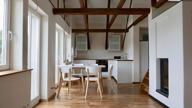 A modern kitchen with wooden beams, a dining area with white chairs, and a fireplace. - Casa Meloni (Bad Sachsa)