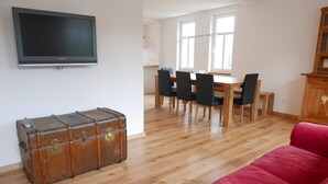 A living room with a red sofa, a wooden dining table with chairs, a television mounted on the wall, and a vintage suitcase on the floor. - Casa Meloni (Bad Sachsa)