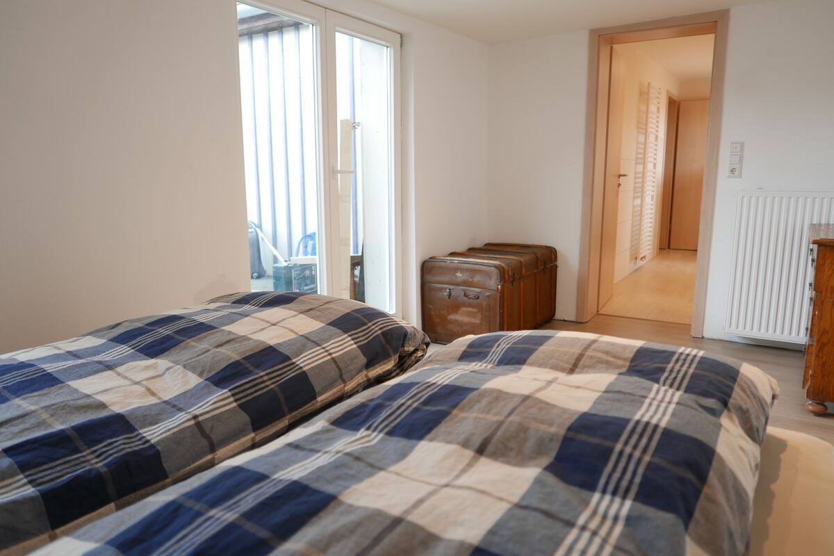 Un dormitorio con dos camas, una puerta corrediza de vidrio, un radiador y una puerta de madera que da a otra habitación.