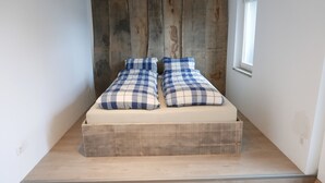 A small bedroom with a wooden headboard, a single bed with plaid bedding, and a small window. - Casa Meloni (Bad Sachsa)