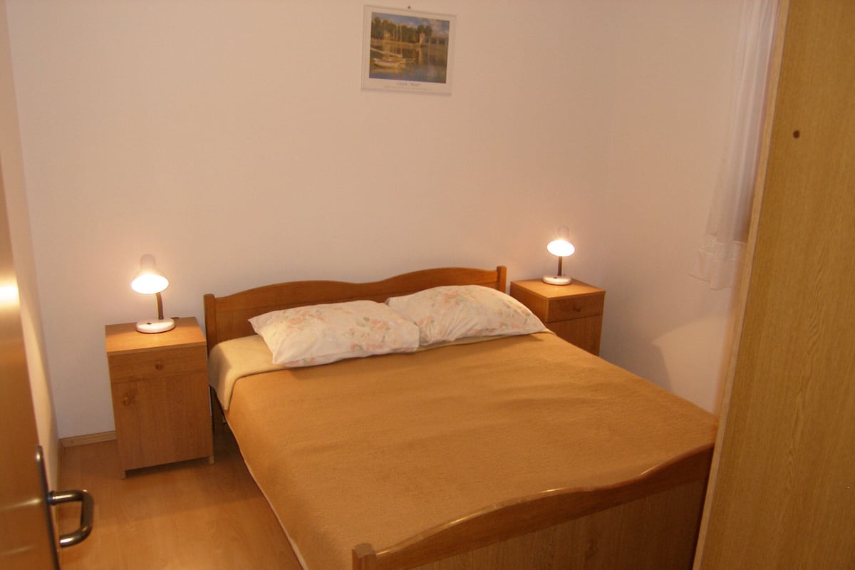 Una cama individual con cabecera y piecera de madera, flanqueada por dos mesitas de noche con lámparas.