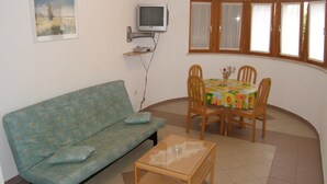 A living room with a sofa, a coffee table, a TV, and a dining table with chairs. - Lorena Apartments (Pula)