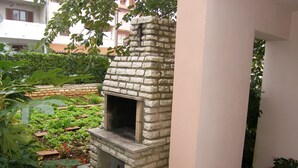 A stone-built outdoor oven, surrounded by a garden with various plants and flowers. - Lorena Apartments (Pula)