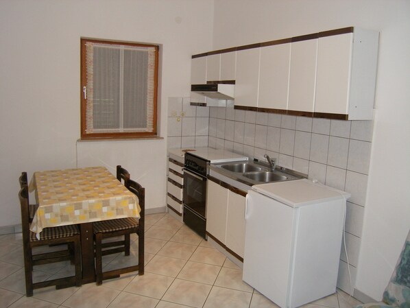 A compact kitchen with a dining table, chairs, a refrigerator, and a sink. - Lorena Apartments (Pula)