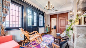 A room with a large window, a chandelier, a wooden rocking chair, a dining table, and a red sofa. - Floral Hotel Yue Tianjin (Tianjin)