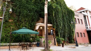 Ein Gebäude mit einer Ziegelwand, die teilweise von Efeu bedeckt ist. Ein Schild mit chinesischen Schriftzeichen, eine Straßenlaterne und Gartenmöbel mit einem grünen Sonnenschirm sind ebenfalls zu sehen.