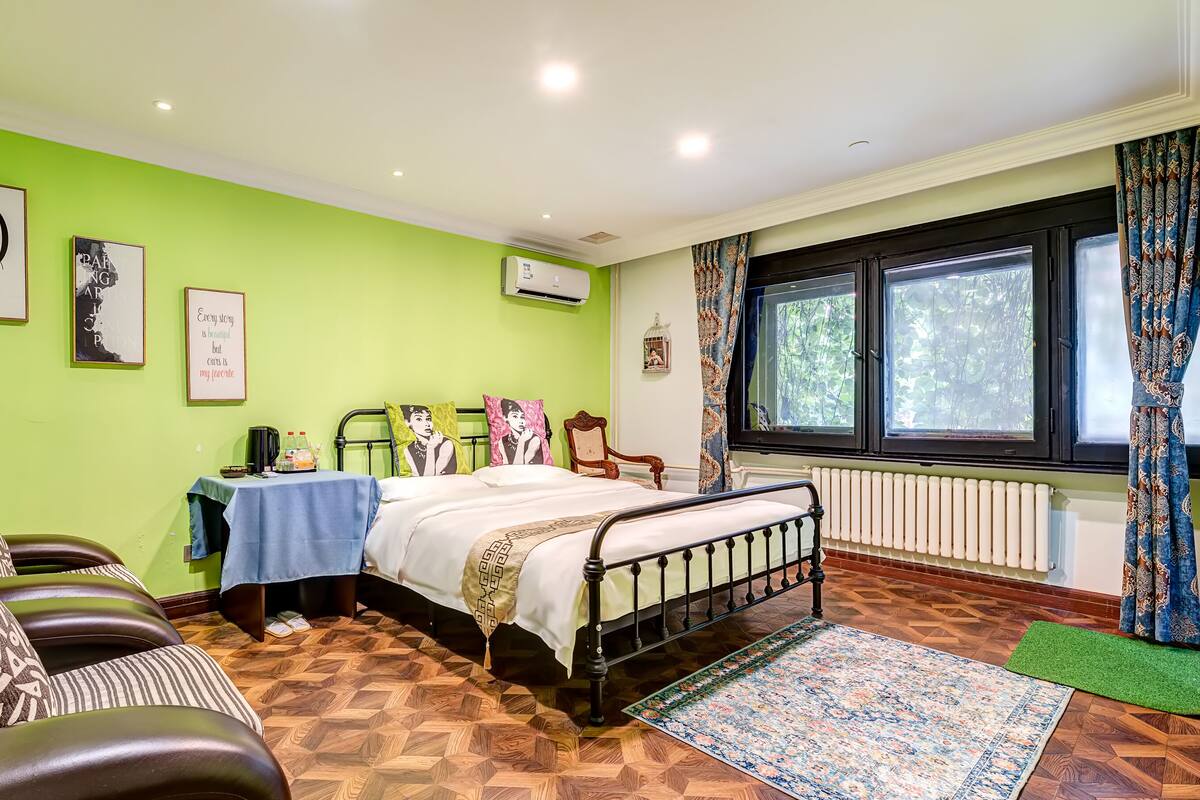 Una habitación con una cama, una silla, una mesa con mantel azul y una ventana con cortinas.