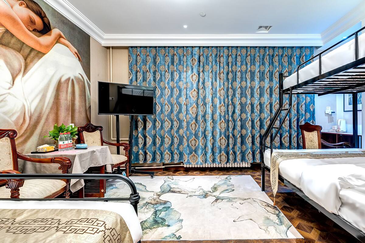 Una habitación de hotel con literas, un escritorio con silla, un televisor y una alfombra estampada.