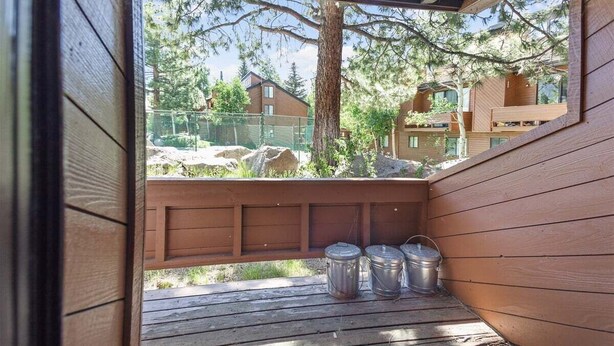 Una terrassa de fusta amb contenidors metàl·lics, amb vista a una zona residencial amb cases i arbres.