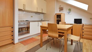 Una cocina moderna con zona de comedor, armarios de madera, horno empotrado y televisor.
