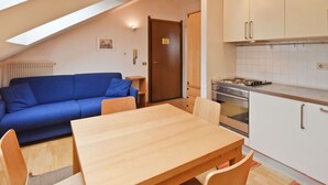 Un espacio habitable compacto con comedor, kitchenette y un sofá azul.
