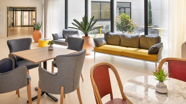 A modern hotel lobby with a seating area, a reception desk, and large windows offering a view of the outside. - DOMITYS - La Majolique (Béziers)