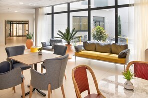 Un hall d’hôtel moderne doté d’un espace salon, d’un comptoir d’accueil et de grandes fenêtres donnant sur l’extérieur.