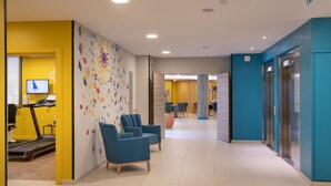 A modern lobby with a treadmill, blue chairs, and a colorful wall mural. - DOMITYS - La Majolique (Béziers)