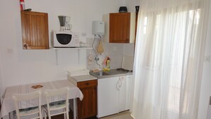 A compact kitchen with a microwave, coffee maker, and a sink. There is a dining table with chairs and a small rug. - Cozy apartment Buterer (Rovinj)