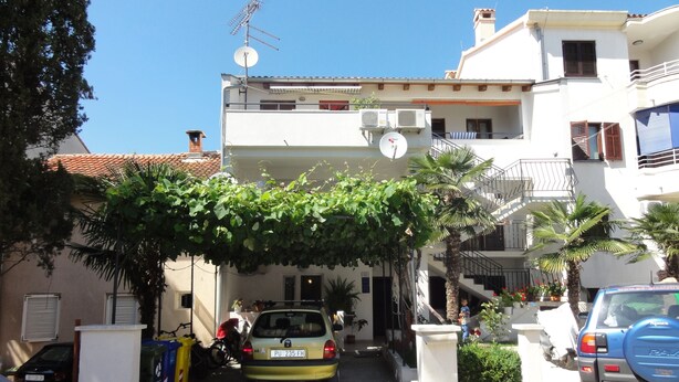 A residential building with a covered entrance, parked cars, and a clear sky. - Cozy apartment Buterer (Rovinj)