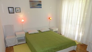 A bedroom with a green bedspread, two bedside lamps, a chair, a nightstand, and a painting on the wall. - Cozy apartment Buterer (Rovinj)