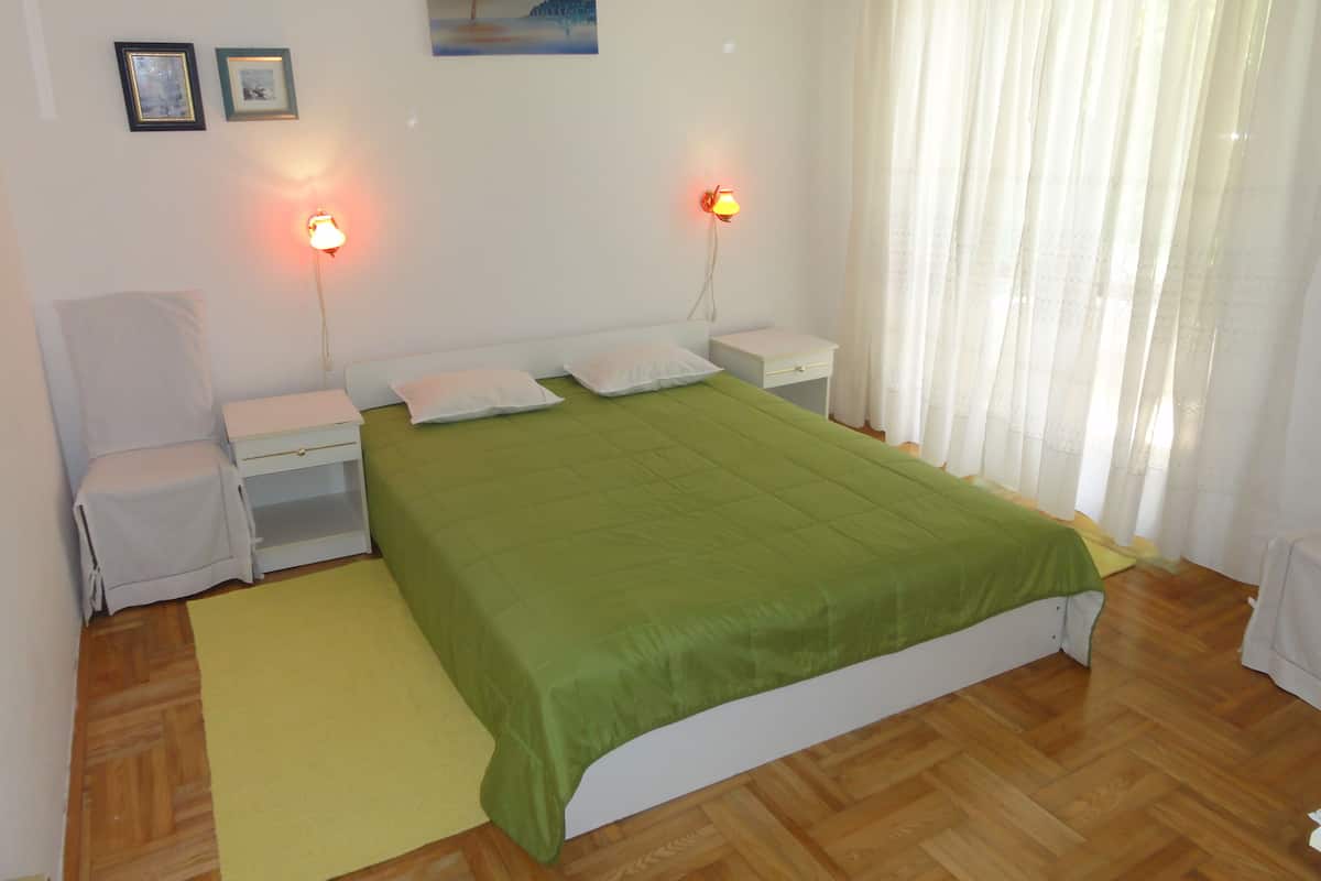 A bedroom with a green bedspread, two bedside lamps, a chair, a nightstand, and a painting on the wall.