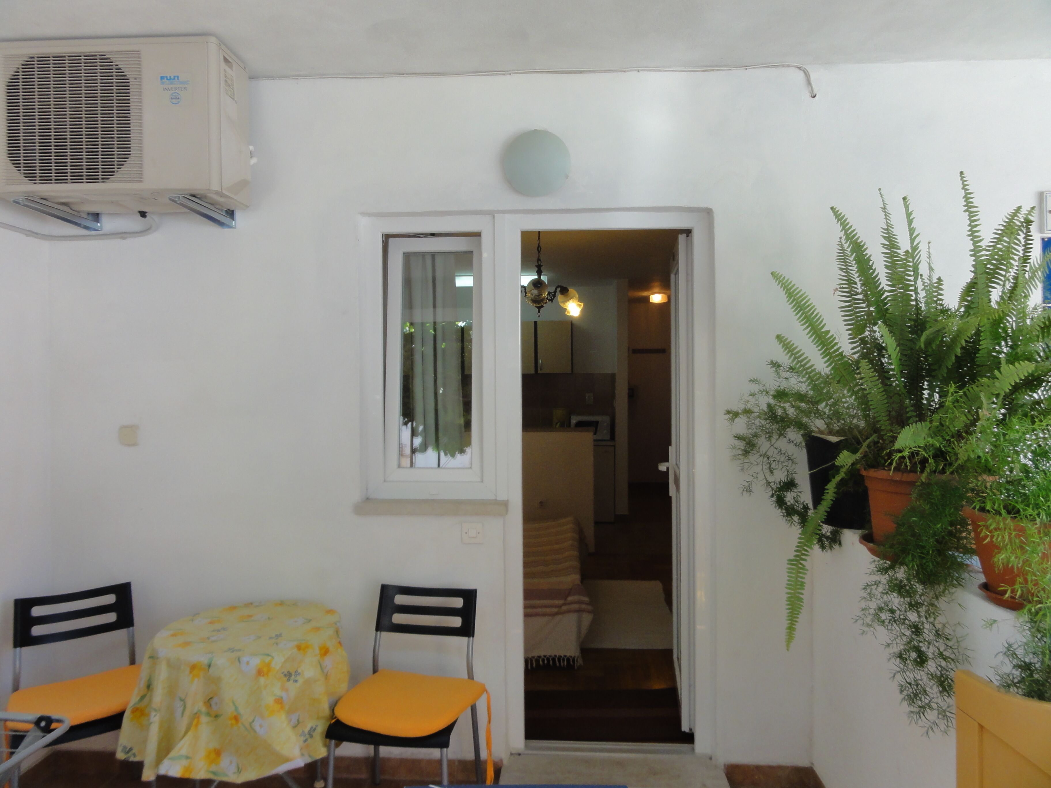 A small dining area with a table and chairs, an air conditioning unit, a door leading to a kitchen, and potted plants.