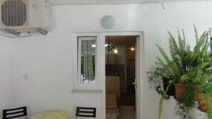 A small dining area with a table and chairs, an air conditioning unit, a door leading to a kitchen, and potted plants. - Cozy apartment Buterer (Rovinj)