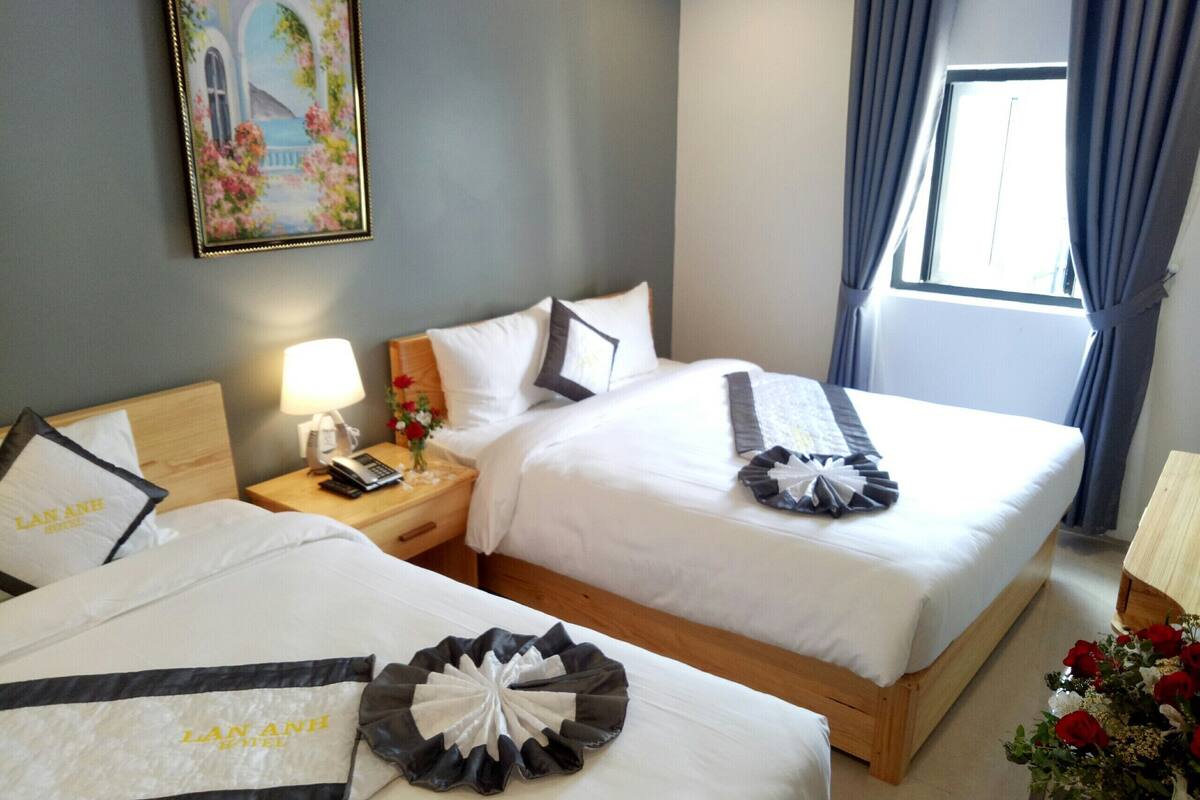 A hotel room with two beds, a nightstand with a lamp, a phone, and a vase with flowers.