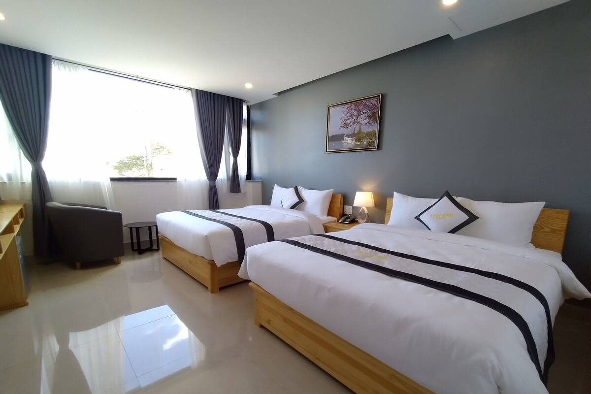A hotel room with two beds, a desk, a chair, a lamp, and a window with curtains.