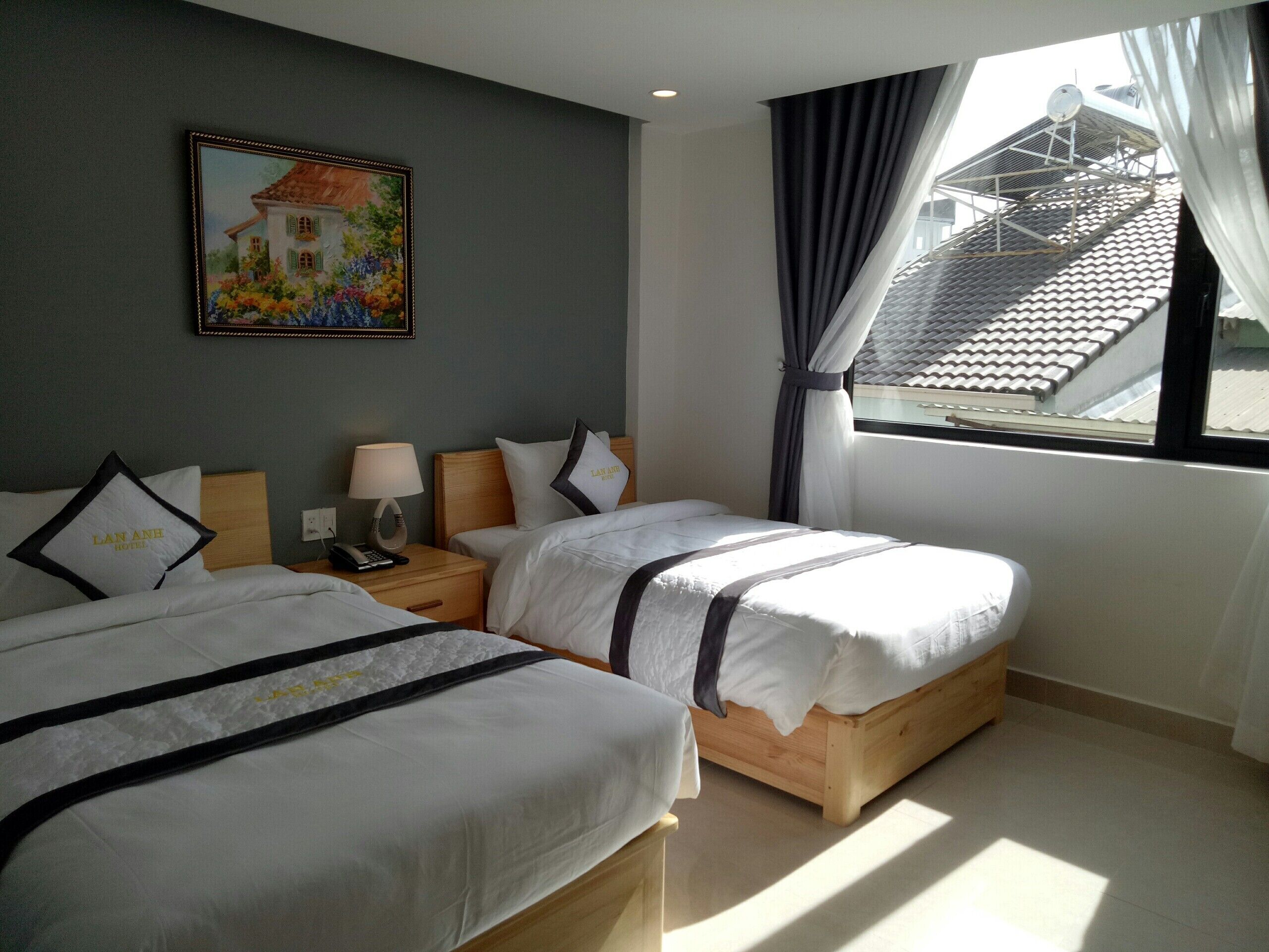 A hotel room with two beds, a painting on the wall, a window with curtains, and a view of the roof.