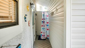 Ein schmaler Balkon mit Holzboden, einer Tür mit Fußmatte und einem Fenster mit Rollläden.