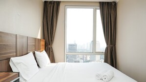 Une chambre d’hôtel avec un grand lit, une tête de lit en bois et une vue sur la ville par la fenêtre.