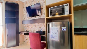 A compact kitchen with a built-in microwave, a refrigerator with a sticker, a red chair, and a TV mounted on the wall.