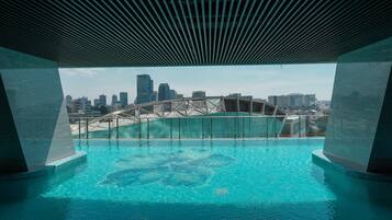 Piscina con vista al horizonte urbano, incluyendo un puente, bajo una estructura de techo moderna.