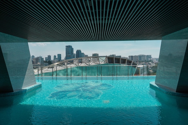 A swimming pool with a city skyline view, including a bridge, under a modern roof structure.
