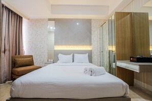 Une chambre d’hôtel avec un grand lit, un fauteuil marron, une table de chevet et un miroir.
