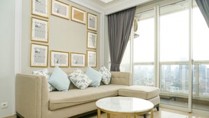 A modern living room with a beige sectional sofa, a round marble coffee table, and a city view through large windows. - Luxurious 2BR with Private Lift at Menteng Park Apartment (Jakarta)
