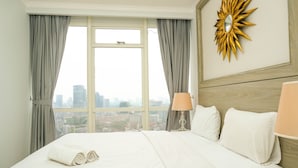 A hotel room with a large bed, two bedside lamps, a sunburst mirror, and a city view through the window. - Luxurious 2BR with Private Lift at Menteng Park Apartment (Jakarta)