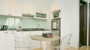 A modern kitchen with white cabinets, a microwave, a refrigerator, and a round table with two transparent chairs. - Luxurious 2BR with Private Lift at Menteng Park Apartment (Jakarta)