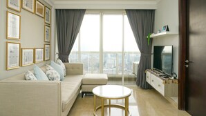 A modern living room with a sofa, a coffee table, a TV, and a balcony with curtains. - Luxurious 2BR with Private Lift at Menteng Park Apartment (Jakarta)