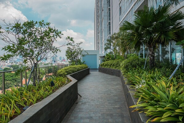 Un chemin bordé de verdure et de bâtiments modernes, qui mène à un immeuble de grande hauteur.