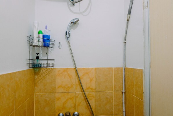 A bathroom with yellow tiles, a shower, a faucet, and a shelf with toiletries.
