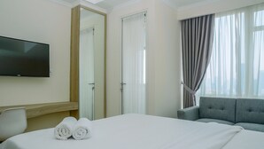 A hotel room with a bed, a TV, a sofa, and a large window with curtains. - Modern and Cozy Studio Menteng Park Apartment (Jakarta)