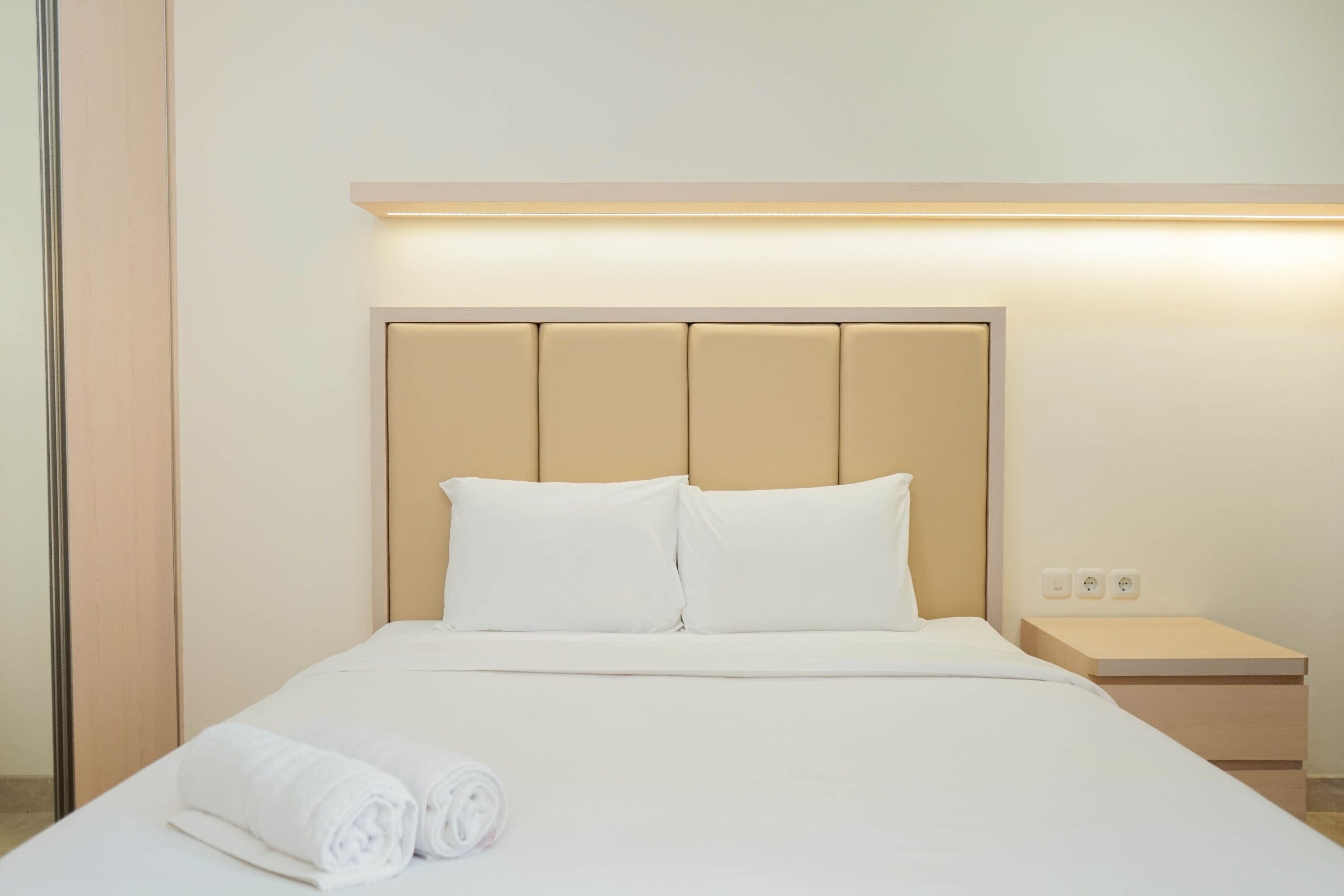 Un lit bien fait, avec du linge de lit blanc et des oreillers, une table de chevet avec une lampe, et une applique murale au-dessus du lit.
