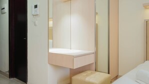 Une chambre d’hôtel avec un lit, une petite table de chevet, un miroir, un téléphone fixé au mur et une porte.