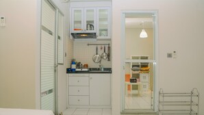 A compact kitchen with white cabinets, a microwave, and a hanging pot rack. - City View Studio Apartment at Menteng Square (Jakarta)